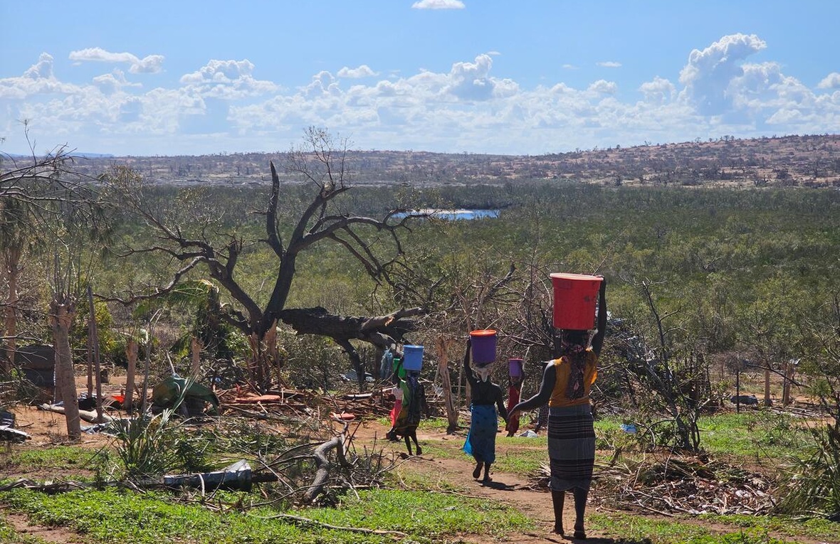 Un grupo de mujeres caminan por un sendero rural cargando baldes de agua en sus cabezas.